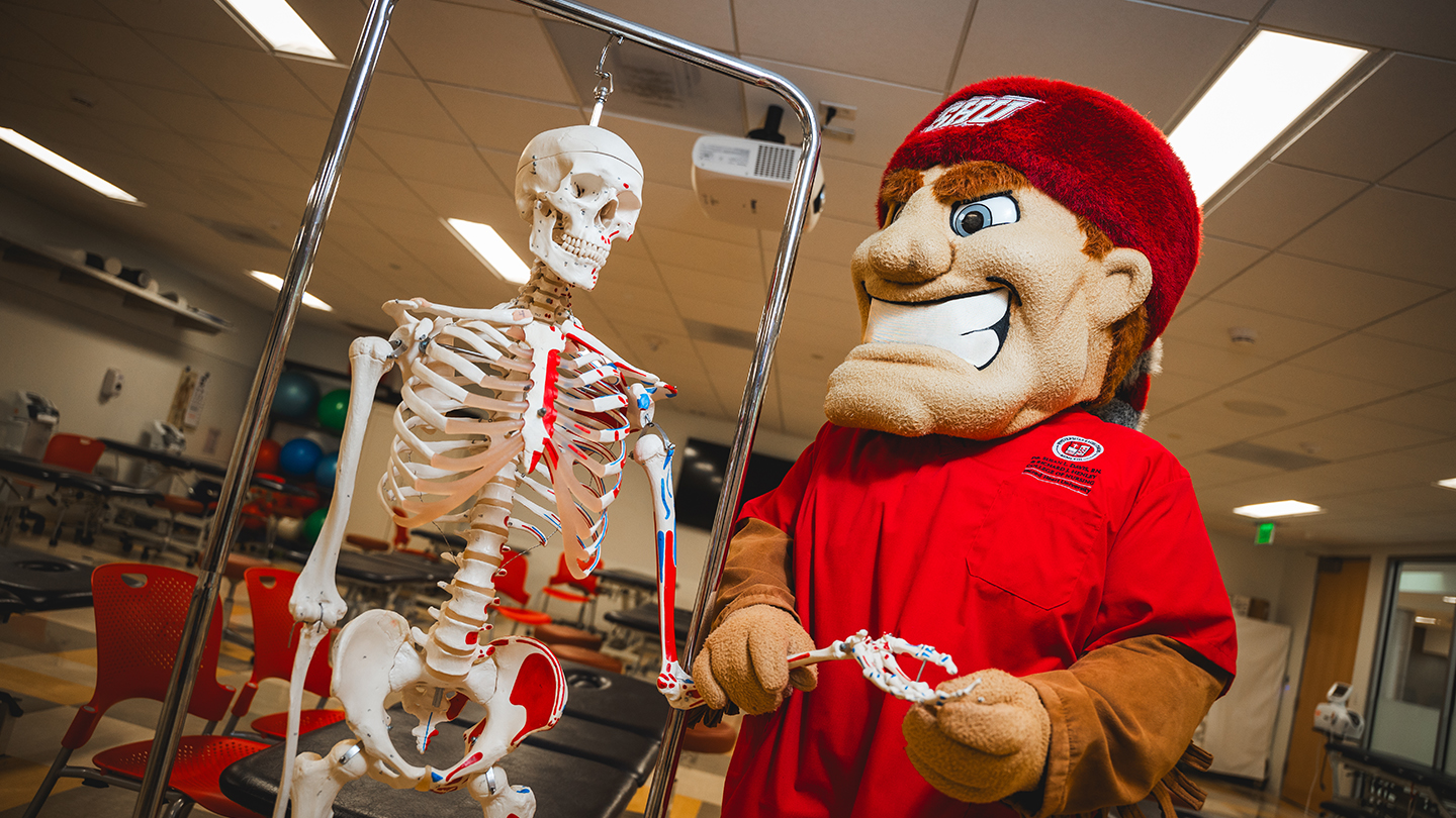 Big Red mascot of Sacred Heart University holds the hand of a skeleton