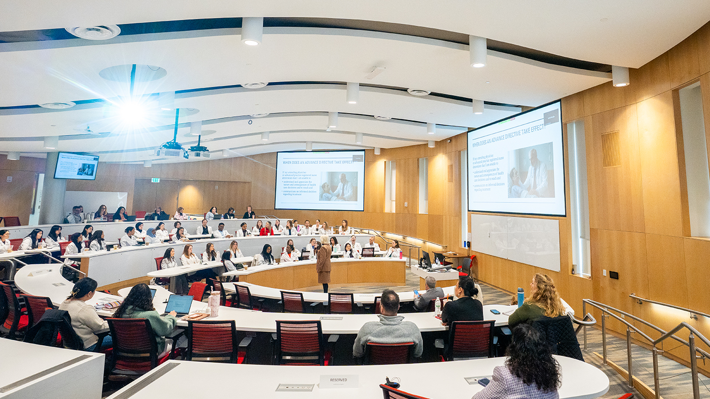 amphitheater-style lecture hall filled with people listening to a guest speaker
