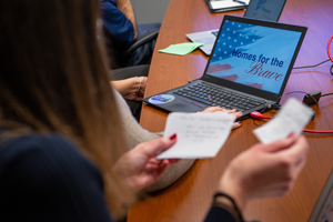 Woman looking at notecards with laptop in background