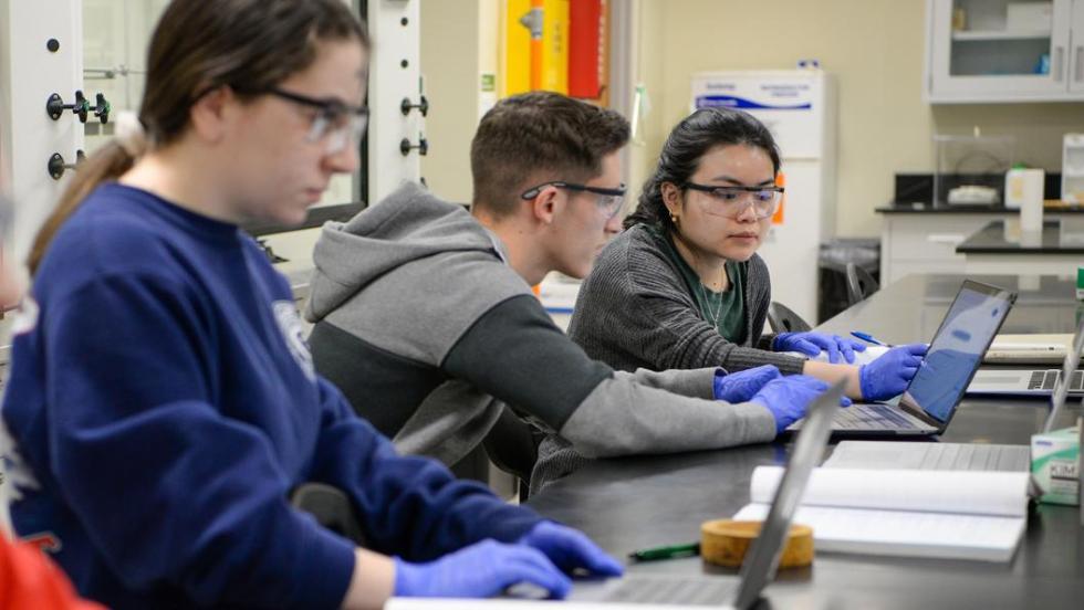 Students in lab gear working on laptops