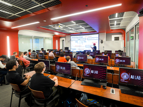 Students in front of computers listening to professor