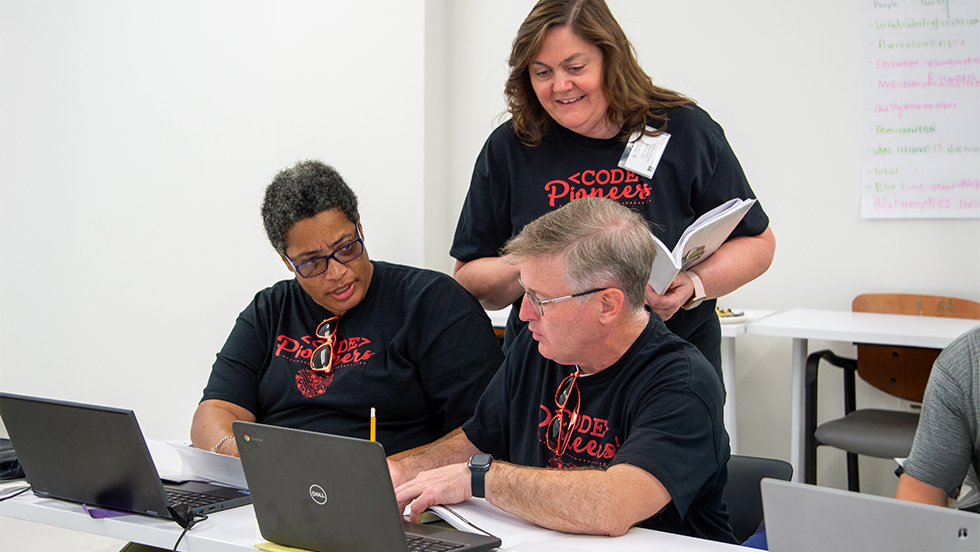 three teachers collaborate during a computer coding conference