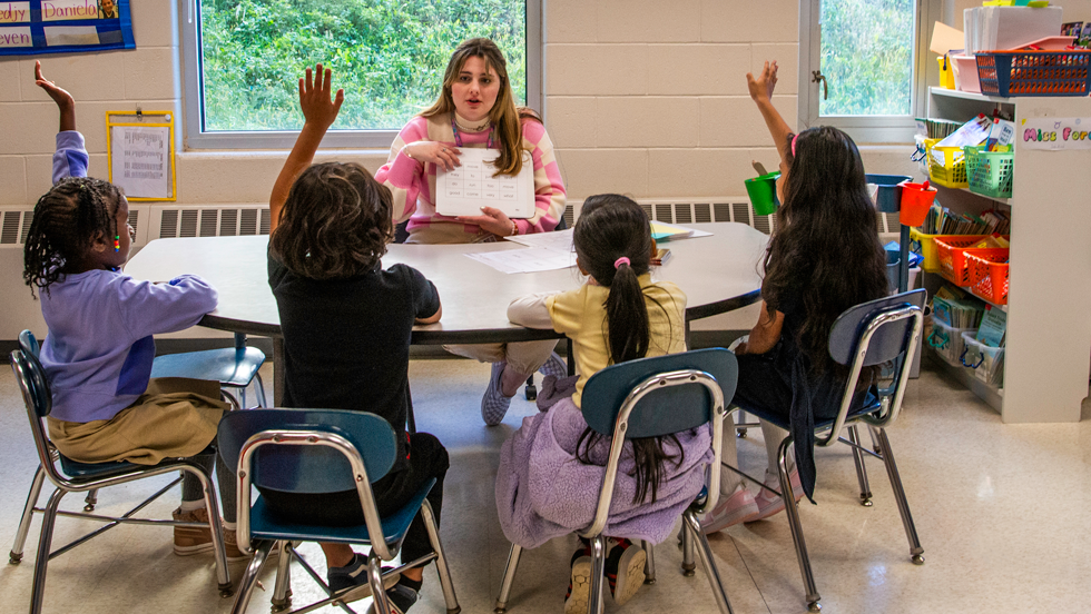 Elementary school students raising hand to answer teachers question