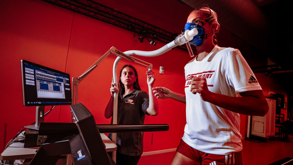 Sport scientist watching athlete run on treadmill with mask on