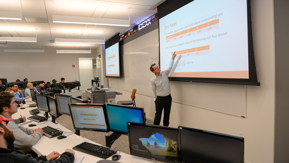 Professor pointing at screen while students are at computers in classroom
