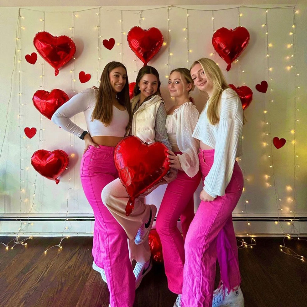 Members of Alpha Delta Pi posing for a photo with heart balloons and twinkling hanging lights in the background
