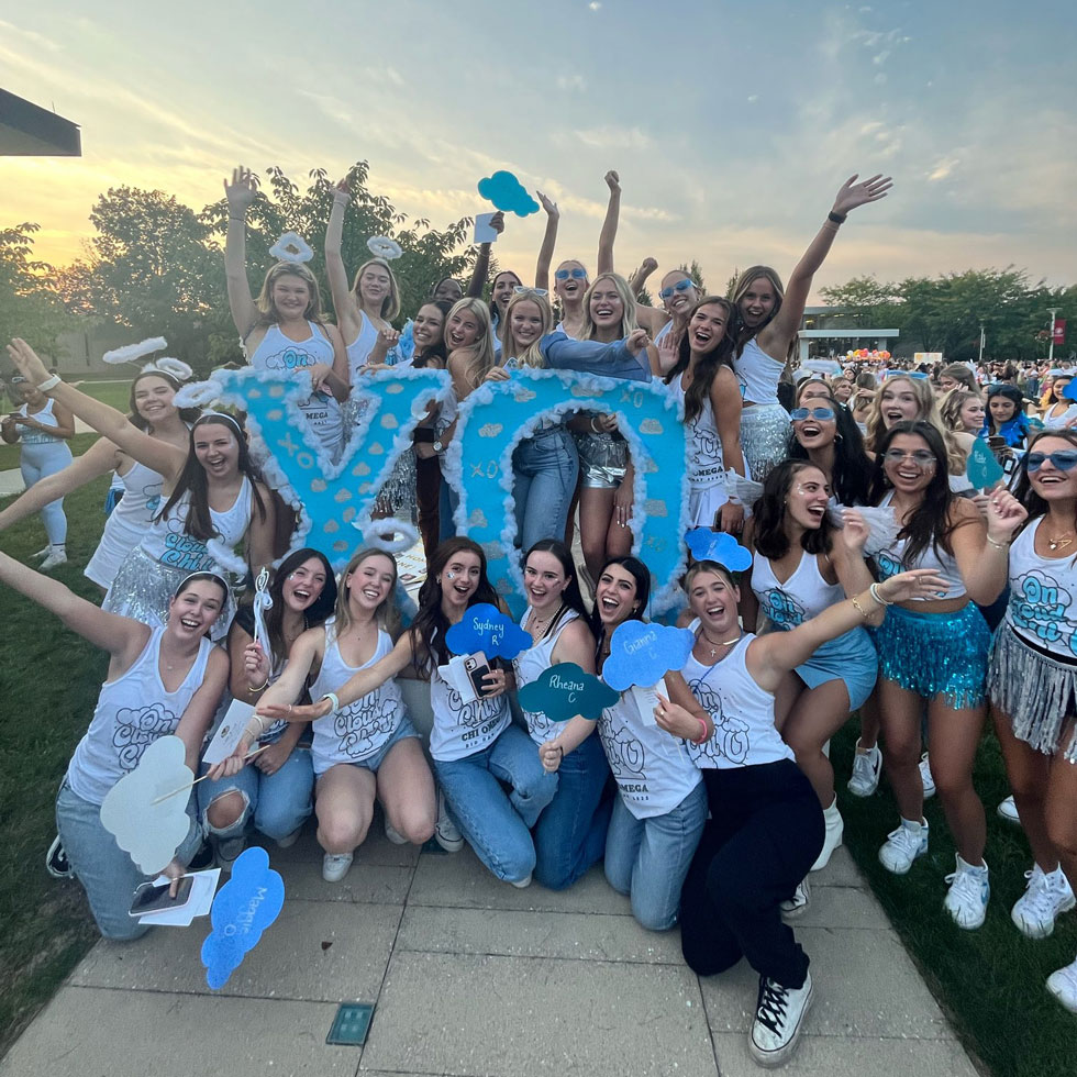 Chi Omega members on bid day smiling with their letters, wearing blue and white