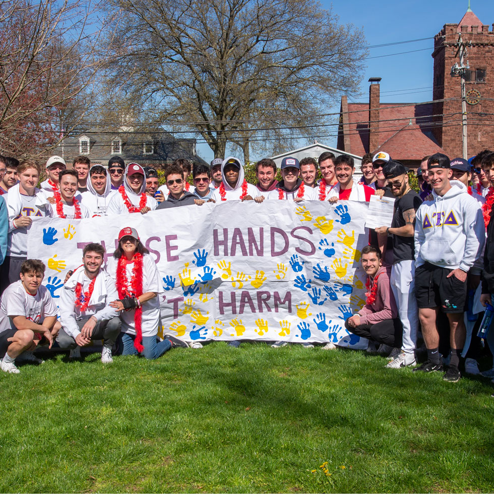 Members of Delta Tau Delta holding a large sign with colorful handprints on it