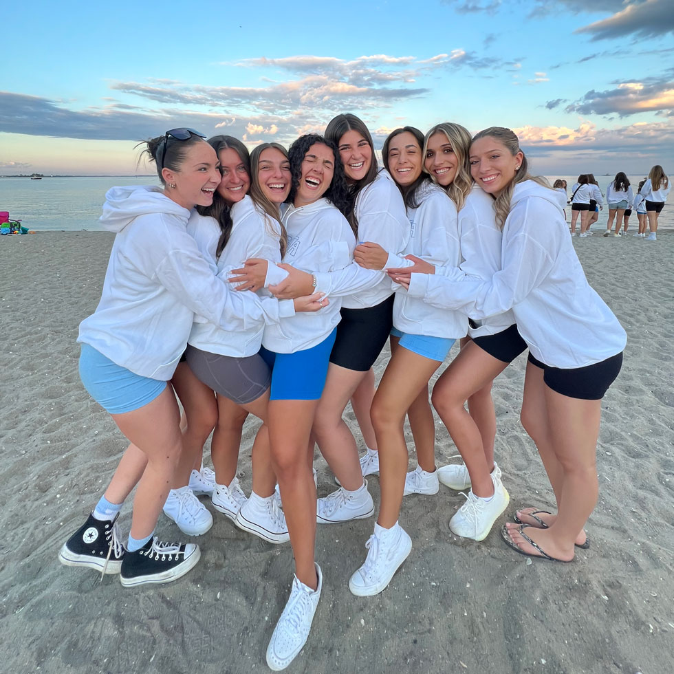 Members of Delta Zeta hugging on a beach, sun setting in the background
