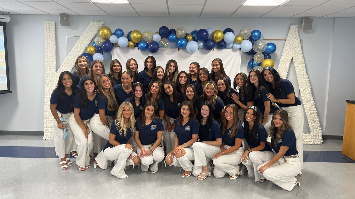 Members of Kappa Delta during recruitment, wearing blue shirt and white pants. Blue and gold balloons in the background