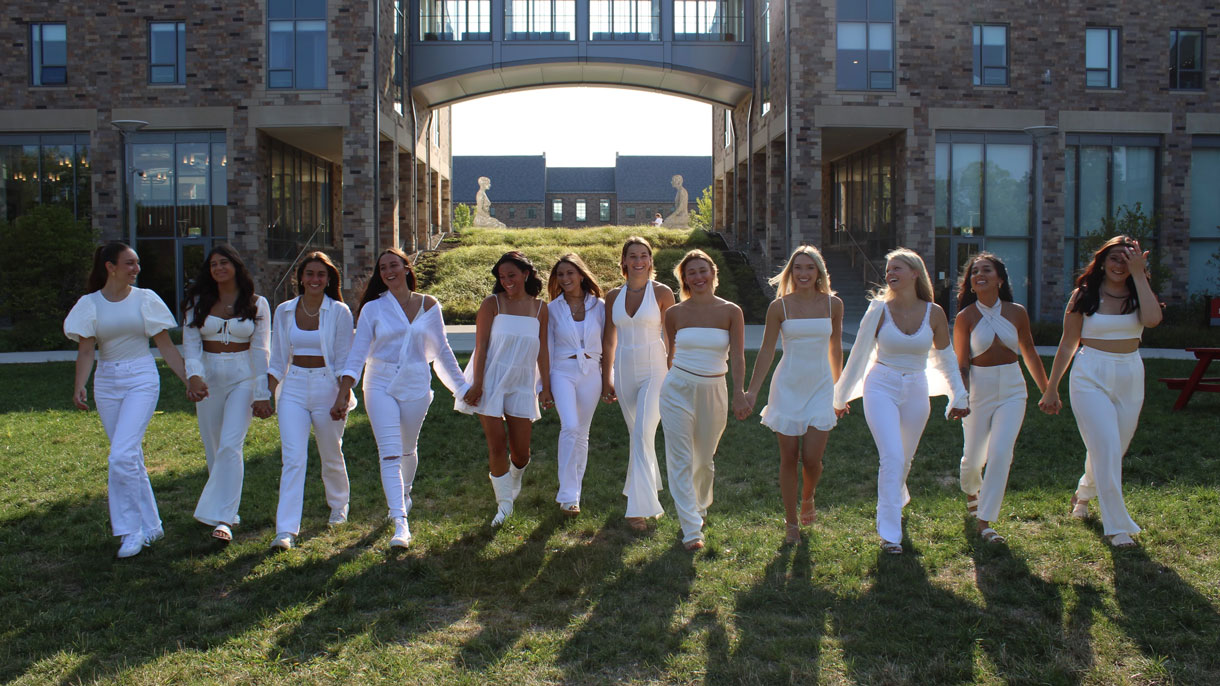 Members of Phi Sigma Sigma wearing white and walking hand in hand