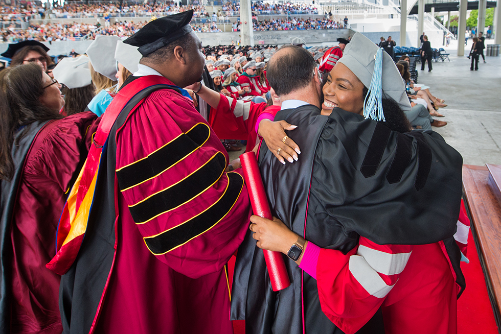 A doctoral graduate hugging a faculty member at a commencement ceremony