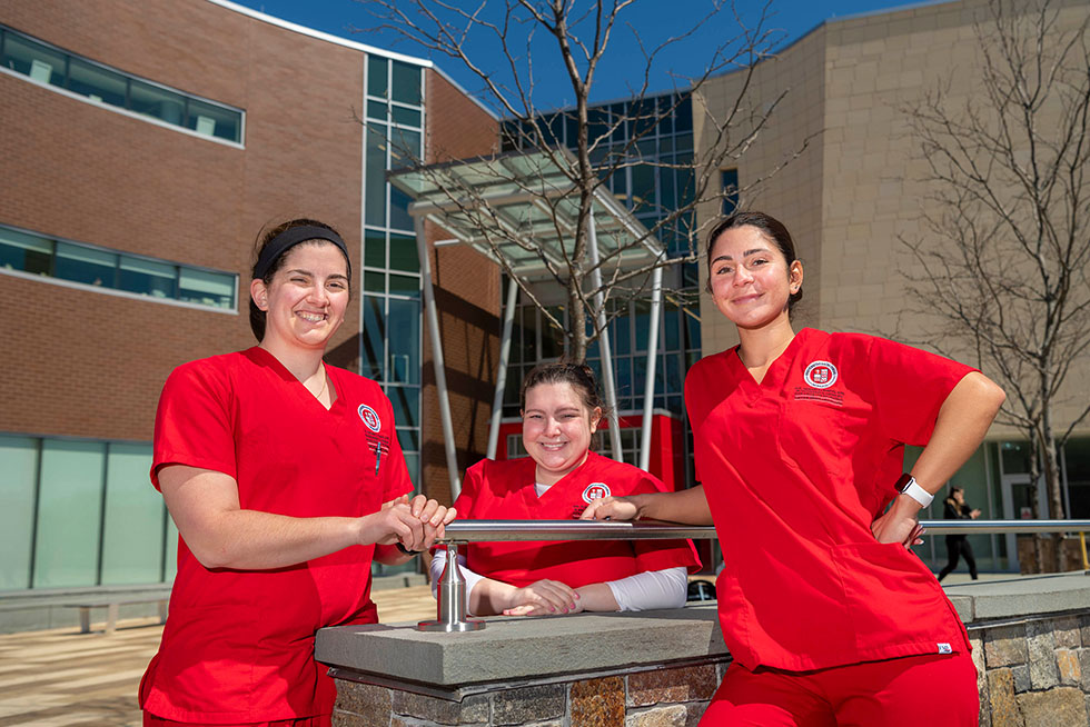 three nursing students in scrubs standing in front of a building