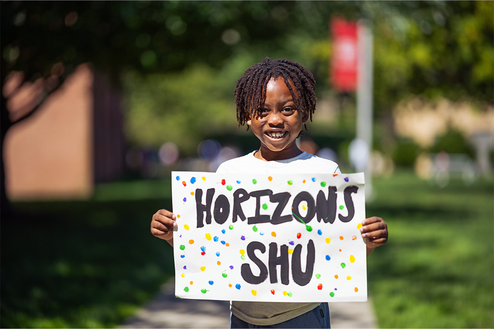 a smiling child holding a Horizons SHU sign