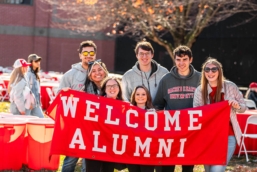 a group of college friends holding up a banner that says welcome alumni