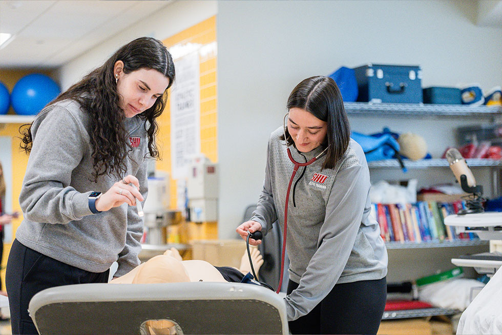 two athletic training college students check the vitals on a medical manikin