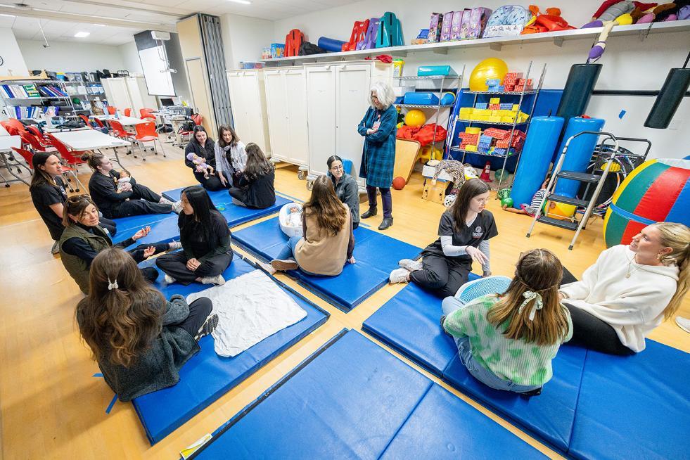 students sitting on floor mats in an occupational therapy class working with infant mannequins
