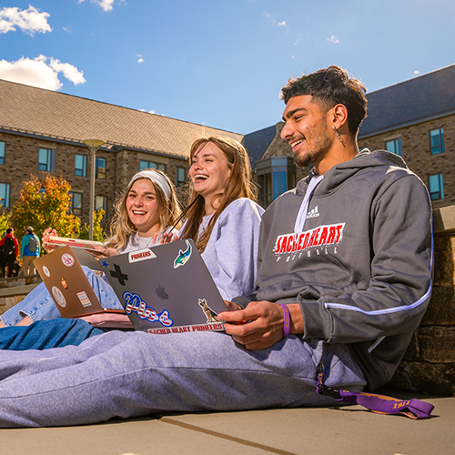 three college students laughing together as they work on laptops