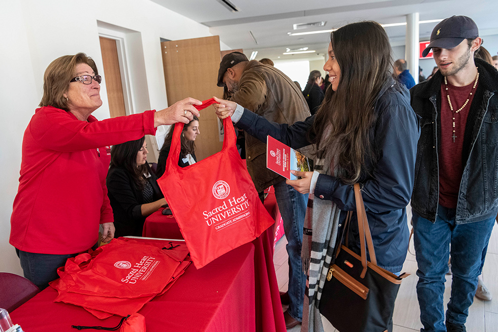 a graduate admissions staff member handing a swag bag to an attendee at a graduate admissions open house event