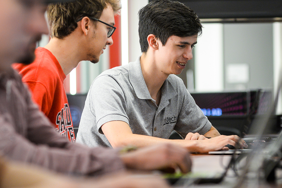 A person smiling while looking at a laptop as another person looks on