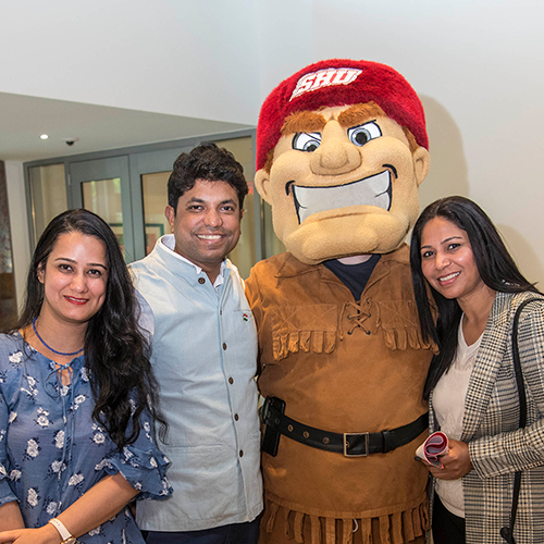 three people posing for a photo with a college mascot