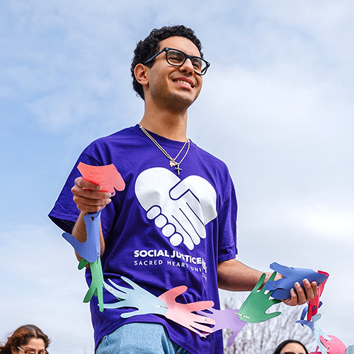 person wearing a social justice week t-shirt and holding a garland made of paper hands interlocked