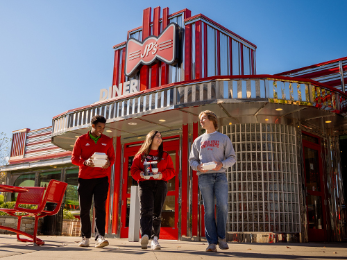 three people walking out of a diner holding to go containers