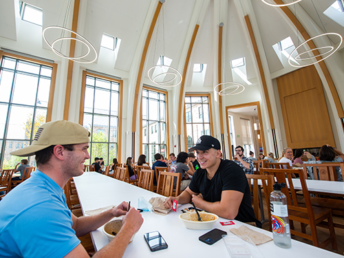 two men sitting at a table eating food and talking