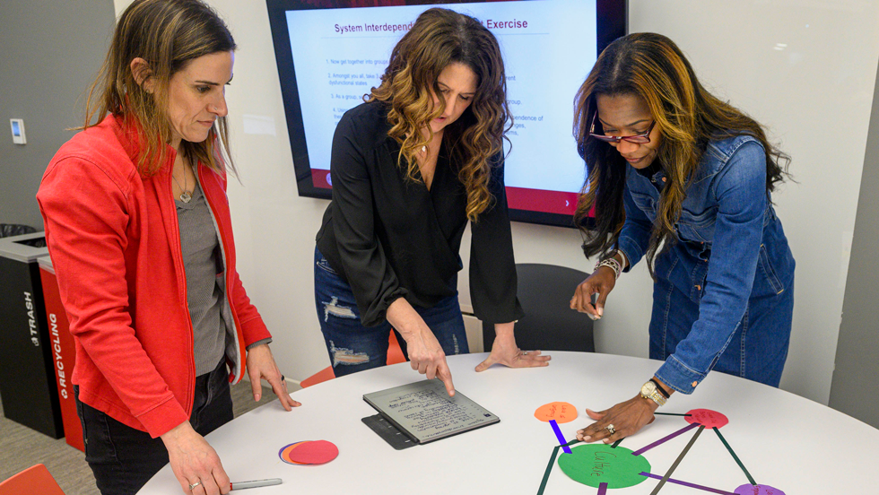 Three women working on a web chart in a classroom