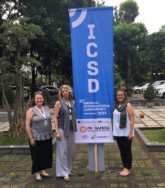 Women smiling for photograph in front of conference banner