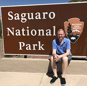 Fred Stula sitting in front of Saguaro National Park sign