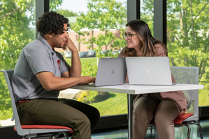 Two students talking and working on laptops