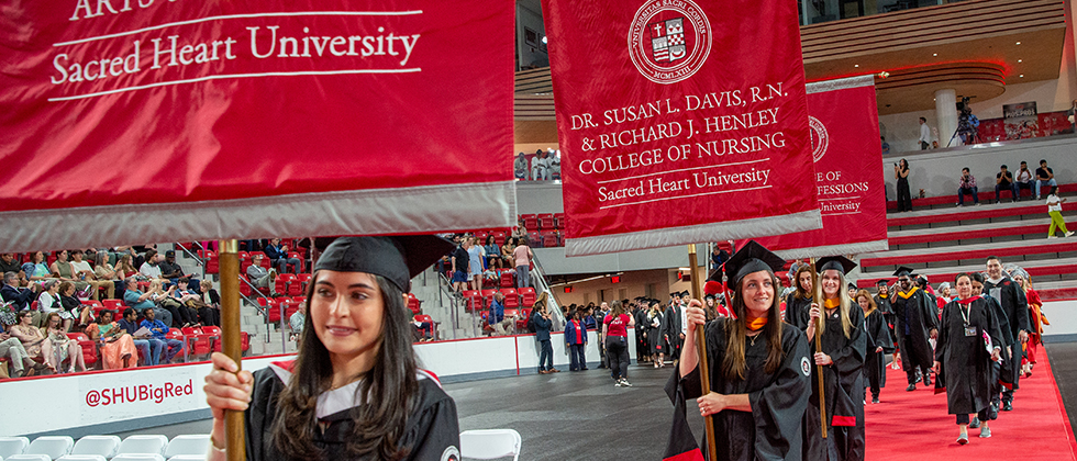 Graduates holding banners walking into Commencement