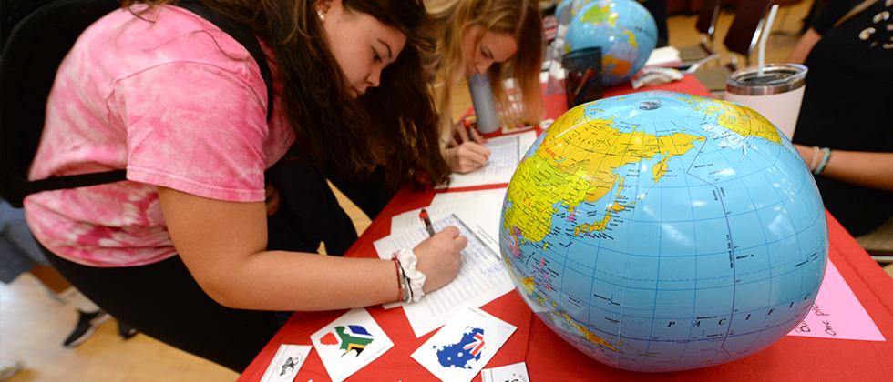 Student filling out paper next to blow up globe