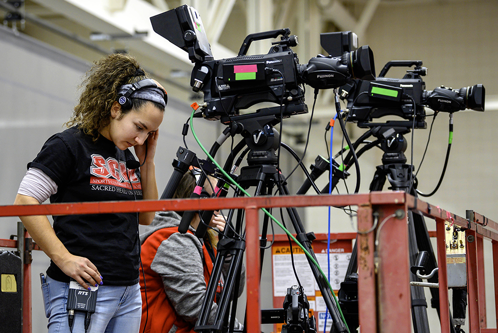 a sports communication student working behind a camera at a basketball game