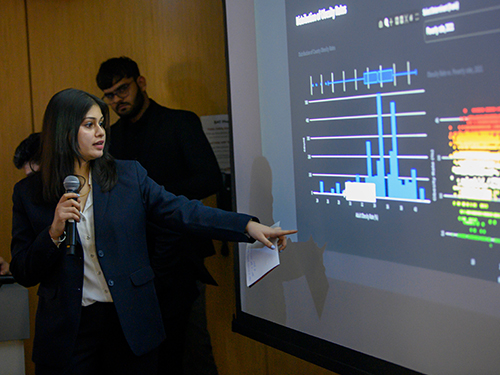 A woman doing a presentation in a class and pointing at data on a screen