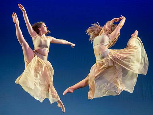 two dancers with flowing costumes jumping in the air