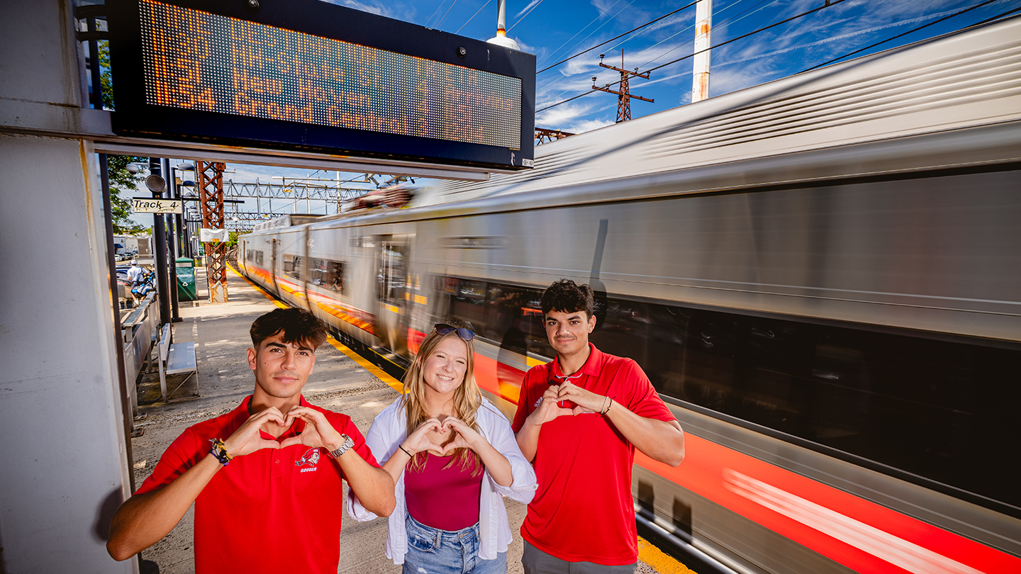 three people making a heart sign with their hands at a train station