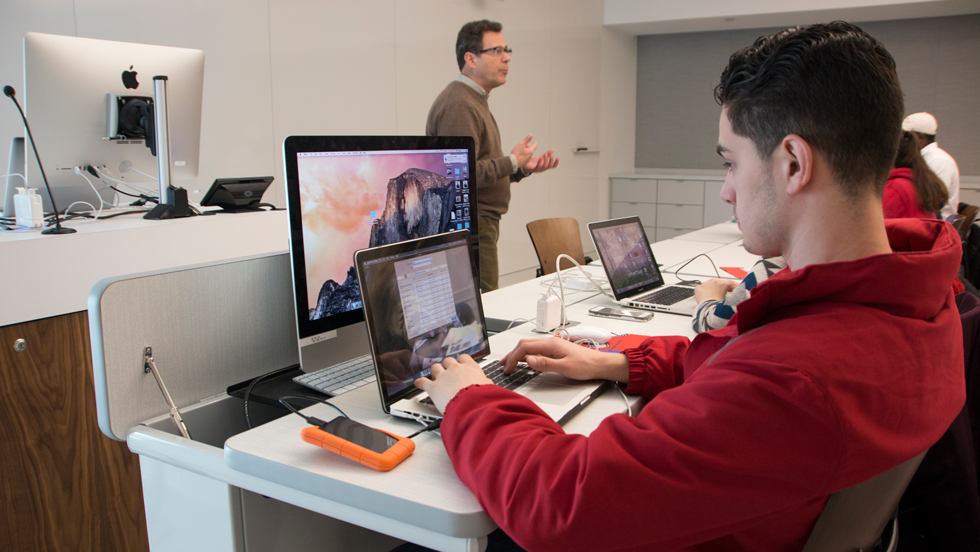 Professor talking to students in class working on laptops