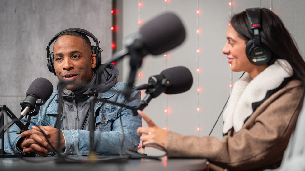 Two people talking into microphones in recording studio