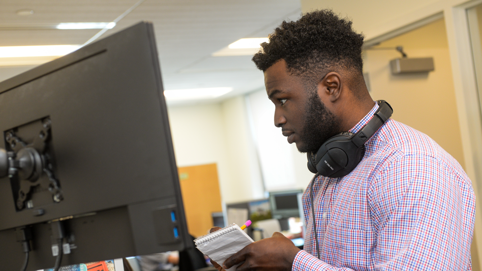 Man looking at computer screen and taking notes