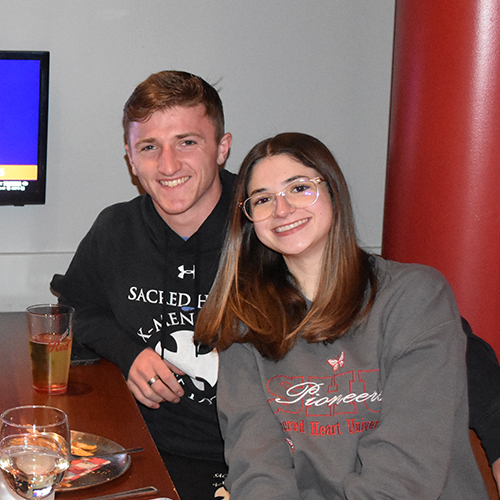 two smiling people sitting at a table with drinks