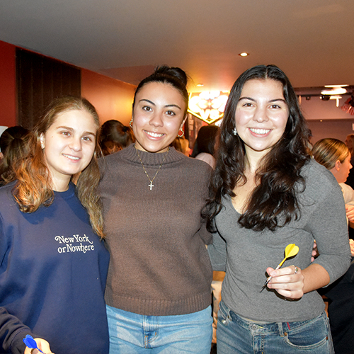 three people smiling and holding darts