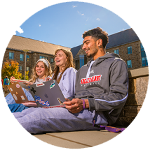 Three college students laughing together while doing work on laptops