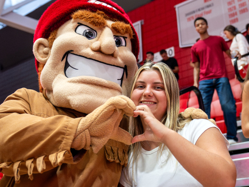 Big Red mascot and person making the shape of a heart with their hands